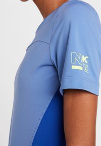 Kortärmad atletisk tröja i ljusblått med mörkblå detaljer. Har en slät yta och en gul logotyp på ärmen.