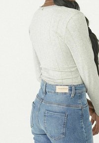 Helles graues Oberteil mit langen �Ärmeln und strukturierten vertikalen Streifen. Hochtaillierte blaue Jeans aus Denim mit Gesäßtaschen und einem Markenlabel.