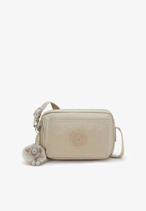 Beige rektangulær crossbody taske i tekstureret materiale, med et rundt logo-patch og en plys abe-nøglekæde. Justerbar rem inkluderet.