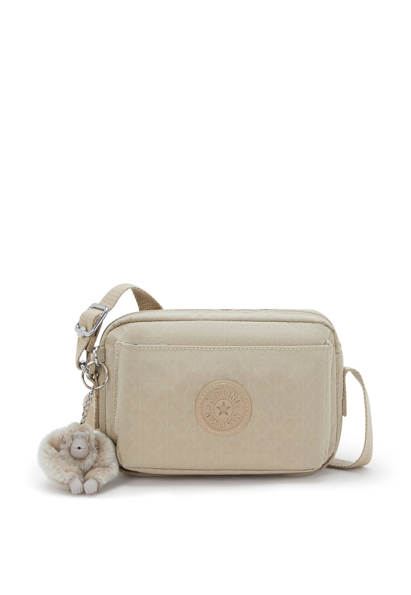 Beige rectangular crossbody bag in textured material, featuring a round logo patch and a plush monkey keychain. Adjustable strap included.