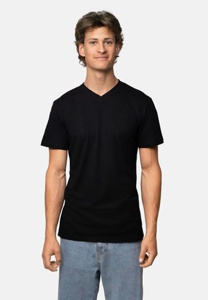 Camiseta negra de cuello en V hecha de una tela suave, con mangas cortas y un diseño ajustado. Combinada con jeans de color azul claro.