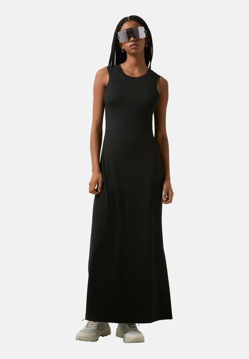 Zwarte geribbelde maxi-jurk met een mouwloos ontwerp, ronde halslijn en enkellange snit. Draag met oversized donkere zonnebril en chunky witte schoenen.