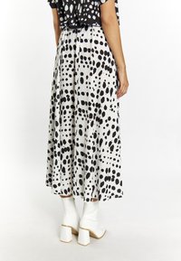 Jupe midi à pois noir et blanc, avec un design fluide et des plis à la taille, associée à des bottes blanches à talons épais.