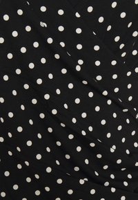Musta kangas, jossa on valkoisia pilkkuja, pehmeä tekstuuri ja laskostettu muotoilu. Huomionarvoista on tasaisesti sijoitetut pyöreät kuviot.