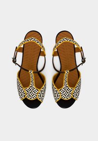 Πέδιλα με ασπρόμαυρο σχέδιο και κίτρινες πινελιές, ανοιχτή μύτη, ρυθμιζόμενο λουράκι αστραγάλου και καφέ υφασμένο εσωτερικό πάτο.