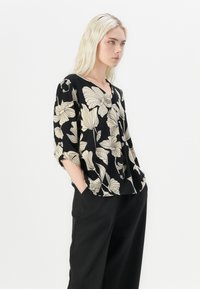 Svart blomstret bluse med korte, rullede ermer, med store beige blomster mønstre, V-hals og en avslappet fasong.