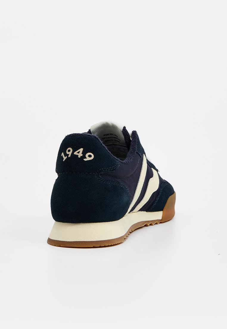 Sneaker blu navy in materiale scamosciato, con accenti beige e collare imbottito. Sul retro è stampato "1949" in bianco. Suola in gomma con motivo antiscivolo.