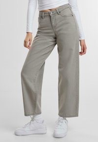 Jeans de pierna ancha en gris claro con cintura alta, confeccionados en denim, que cuentan con cierre de botón y bolsillos laterales. Combinados con zapatillas blancas.