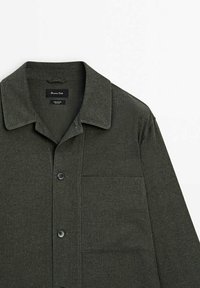 Donkergroen overhemd met knoopsluiting in een gestructureerde stof. Voorzien van een puntige kraag, een enkele borstzak en zwarte knopen. Stijlvol en functioneel ontwerp.
