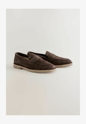 Hnedé semišové mokasíny so šitým vzorom, plochou gumovou podrážkou a výrazným remienkom cez vrch. Hladká textúra a ležérny tvar.