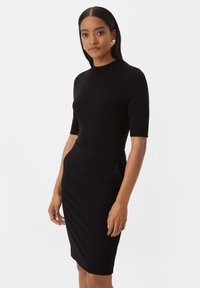 Haut noir à manches courtes associé à une jupe crayon noire à la longueur du genou. Tissu lisse avec une silhouette ajustée et de subtiles poches latérales.