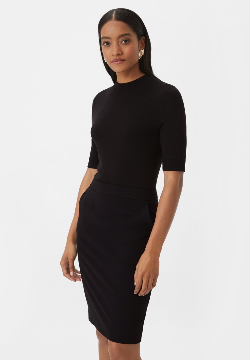 Haut noir à manches courtes associé à une jupe crayon noire à la longueur du genou. Tissu lisse avec une silhouette ajustée et de subtiles poches latérales.