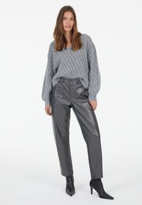 Grau gestrickter Pullover mit strukturiertem Muster, kombiniert mit hochtaillierten grauen Lederhosen mit aufgesetzten Taschen und spitzen schwarzen Absätzen.