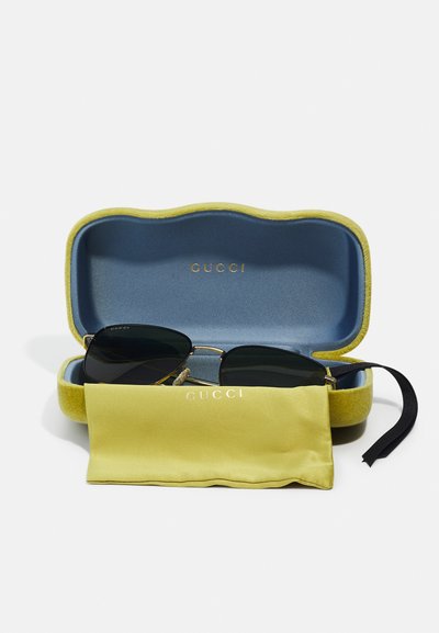 Mustad mustrik pruunide raamidega mustad prillid, mis on väljas rohelises ja sinises karbis. Kaasas kollane siidist kott, millel on "GUCCI" logo.