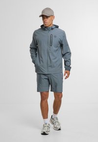 Light grey waterproof jacket with hood, black zipper, and pocket; paired with matching shorts and sneakers, on a plain white background.