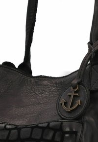 Bolso de cuero negro con superficie texturizada, presenta un emblema de ancla metálico y correas suaves. Costuras y acentos distintivos visibles.