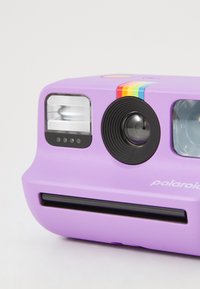 Polaroid fotoaparát v levandulové barvě, s duhovým pruhem, kulatým objektivem, dvojitým bleskem a černými akcenty. Kompaktní design s filmovým slotem ve spodní části.