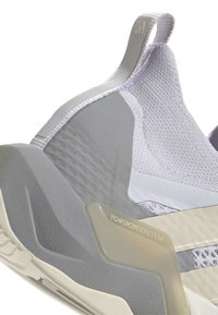 Talons de baskets athlétiques blancs et gris avec empeigne en maille texturée, languette de traction et détail de support beige « TORSION SYSTEM » sur la semelle intermédiaire.
