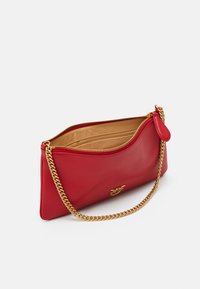 Pochette en cuir rouge avec un design incurvé, une bandoulière en chaîne dorée et une fermeture éclair. L'intérieur est doublé de beige et comprend plusieurs compartiments.
