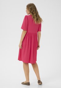 Robe rose, mi-longue, avec des manches courtes et amples, un corsage ajusté et une taille froncée, fabriquée à partir d'un tissu texturé. Design sobre.