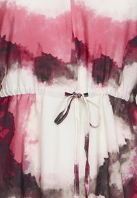Gros plan sur un tissu à motif tie-dye rose, bordeaux et gris foncé, avec une ceinture froncée et un cordon à nouer.