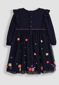 Ärmelloses Kleid in Marineblau mit langen Ärmeln, Rüschenschultern, Knopfverschluss und einem Tüllrock, der mit floralem und sternförmigem Stickereien in verschiedenen Farben verziert ist.