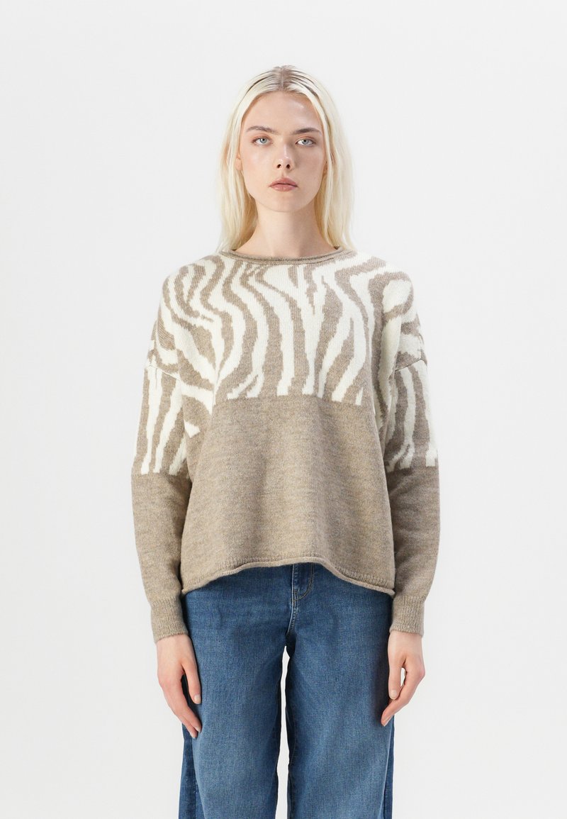Beige and cream striped sweater made of soft knit material, featuring a relaxed fit, round neckline, and long sleeves. Paired with denim jeans.