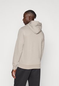 Ανοιχτό μπεζ φούτερ με υφή, ρυθμιζόμενο κουκούλι και ριμπ μανσέτες. Φορεμένο με σκουρόχρωμο παντελόνι, εμφανίζοντας άνετη εφαρμογή και κανονικό σχεδιασμό.