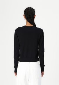 Sort strikket sweater med lange ærmer, rund hals og ribbet kant, båret med hvide højtaljede bukser. Ren, tætsiddende silhuet.