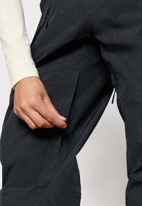 Μαύρο αδιάβροχο παντελόνι με τσέπη με φερμουάρ και κλείσιμο με κουμπί, που διαθέτει λείο υφή και εφαρμοστή σχεδίαση για λειτουργικότητα.