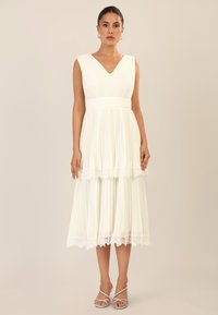 Vestido blanco con pliegues y escote en V, con borde de encaje en el dobladillo y una silueta fluida. Acentuado con una cintura ceñida y un diseño sin mangas.