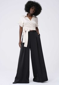 Beige wikkeltop met korte mouwen en een strikdetail, gecombineerd met zwarte brede broek met plooien en zijzakken.
