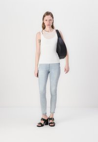 Top a coste bianco, jeans skinny azzurri chiari e sandali neri con tacco e dettagli in oro. La modella porta una borsa a tracolla nera.