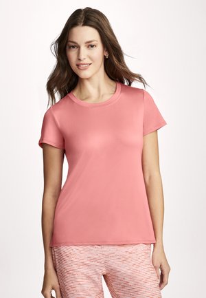 Woman with long brown hair wearing coral short-sleeve shirt and pink and white striped pants, smiling against a plain white background.