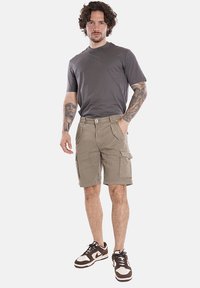 Pantaloni cargo beige con molte tasche e una maglietta a girocollo grigia. Indossati con scarpe da ginnastica marroni e bianche. Design a vestibilità dritta.