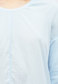 Jasnoniebieski, teksturowany top z zaokrąglonym dekoltem i szwami, z gładkim, miększym materiałem na rękawach.