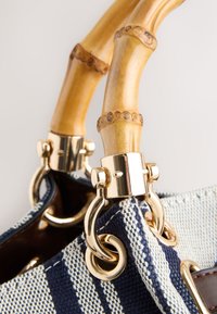 Poignées en bambou fixées avec des garnitures dorées à un sac à main en tissu tissé rayé bleu et blanc.