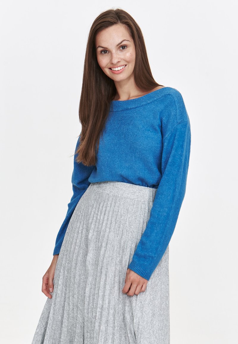 Niebieski wrabiany sweter z długimi rękawami, w połączeniu z szaro plisowaną spódnicą. Sweter ma szeroki dekolt i miękką fakturę.