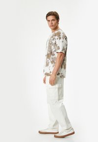 Tie-dye t-shirt i creme og brunt, korte ærmer, afslappet pasform. Parret med hvide cargo bukser med store sidelommer og en solid tekstur.