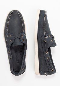 Navy blue boat shoes made of textured leather with white stitching, featuring gold eyelets and a beige sole.