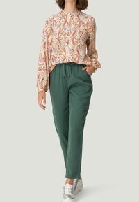Blusa de manga larga con estampados de flores en tonos naranja, rojo y azul paisley; combinada con pantalones cargo verdes; look informal complementado con zapatos plateados.