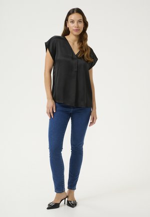 Black satin blouse with a V-neck and short sleeves, paired with blue skinny jeans and black pointed-toe heels with decorative accents.