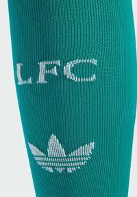 Teal Sportsocke mit gerippter Textur, versehen mit weißen gestickten "LFC"-Buchstaben und einem stilisierten weißen Markensymbol darüber.