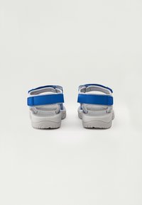 Zili un pelēki sandaļi ar regulējamiem siksniņām, mīkstiem ieliktņiem un teksturētām gumijas zolēm, ar drošu aizmugures dizainu.