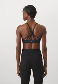 Črn športni nedrček z aktivnim dizajnom in trakovi na hrbtu, izdelan iz elastičnega materiala z gladko teksturo. Pas je visok in rebrast.