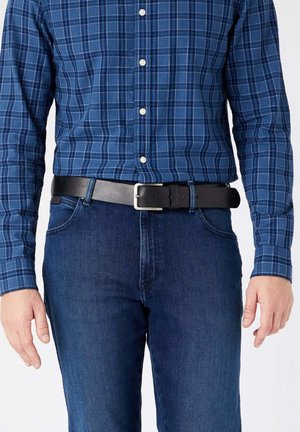 Blåternet skjorte med hvide knapper, parret med mørk denim jeans og et sort læderbælte med en sølvspænde.