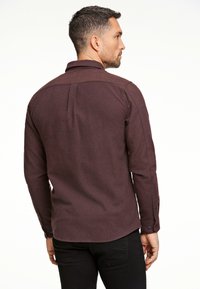 Ruskea flanellipaita, jossa on kaulus, pitkät hihat ja napilliset hihansuut. Ominaisuutena on teksturoitu kangas ja suora helma, jossa on takana kaarroke-sisustus.