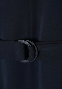 Námořnické šaty z látky se širokým páskem s černou kulatou kovovou sponou a uzlovým detailem, který zdůrazňuje texturu a design.