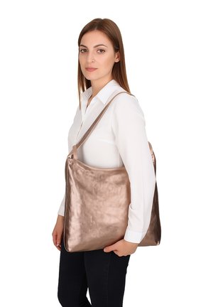 Sac en toile métallique rose doré avec une texture lisse, grande taille, et une seule bandoulière, tenu dans la main d'une femme sur fond blanc.