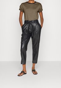 Brun texturerad t-shirt med rullade ärmar, tillsammans med höga svarta läderbyxor och platta svarta sandaler med guldaccenter.